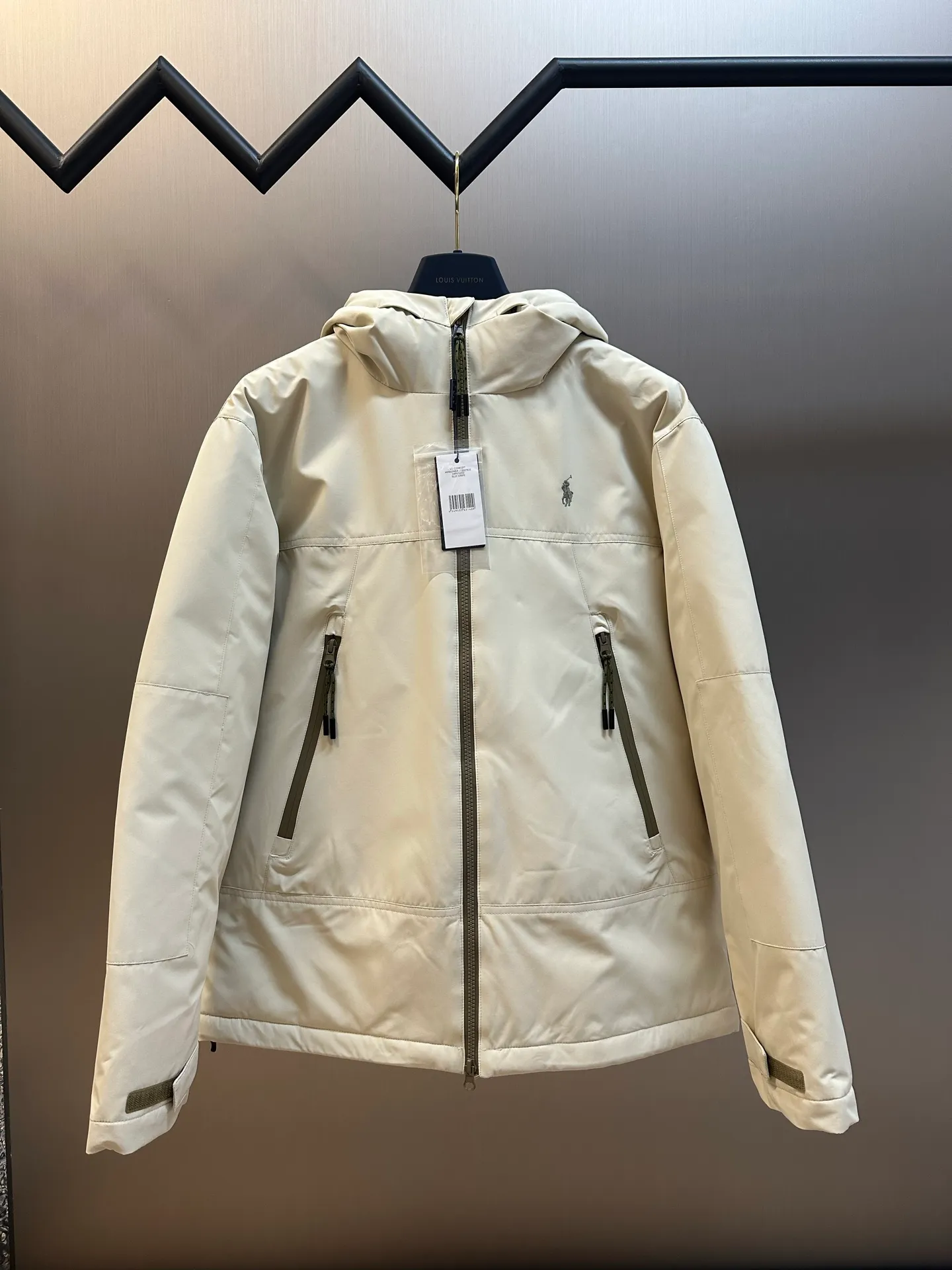 P970 Ralph Lauren logo hooded down jacket. The density of high-density nylon taffeta is about 210T-300T. The surface is smooth and slightly matte. It has excellent windproof and waterproof performance (with DWR water-repellent treatment). It has strong wrinkle resistance and is easy to care for. It is in line with the positioning of American casual "durable and practical".  The inner lining is made of 100% polyamide. The high-density and tight weaving process prevents fine lint from getting out of the gaps in the fabric. The smooth surface improves the putting on and taking off experience, and the excellent wear and tear resistance ensures damage caused by frequent use, while the light and soft texture does not affect the overall weight.  It uses 90 white duck down with a weight of 220g to ensure excellent thermal insulation performance. After strict screening and processing, the velvet is not easily drilled, ensuring durability. The classic jacket has a slightly loose fit, with slightly dropped shoulder lines (the shoulder width is 1-2cm wider than the standard fit). The length reaches the hips, and the sleeves are slightly tapered straight sleeves, taking into account freedom of movement and casual style.  The adjustable Velcro on the cuffs allows you to freely adjust the tightness according to the thickness of your wrist and personal preferences, effectively preventing cold wind from intruding, and improving the warmth performance. Two zippered pockets on the front are convenient for placing frequently used items, and the zipper design ensures that items are not easily lost. A built-in pocket on the left side of the chest provides a safe storage space for some small private items.  The drawstring design at the hem allows you to adjust the shape of the jacket according to your body shape and dressing needs. Whether it is loose and casual or slim and neat, you can easily control it.  Polo horse logo on the left chest: flat satin stitch embroidery (satin embroidery), using 100% polyester high color fastness embroidery thread (the color number is consistent with the brand's standard red color card), the stitch density is 12-15 stitches/cm, the outline of the horse logo is clear, and the details of the rider and horse are burr-free. Precise positioning through the template (12cm from the bottom of the collar and 8cm from the placket) ensures symmetry and centering.  size：s m l xl